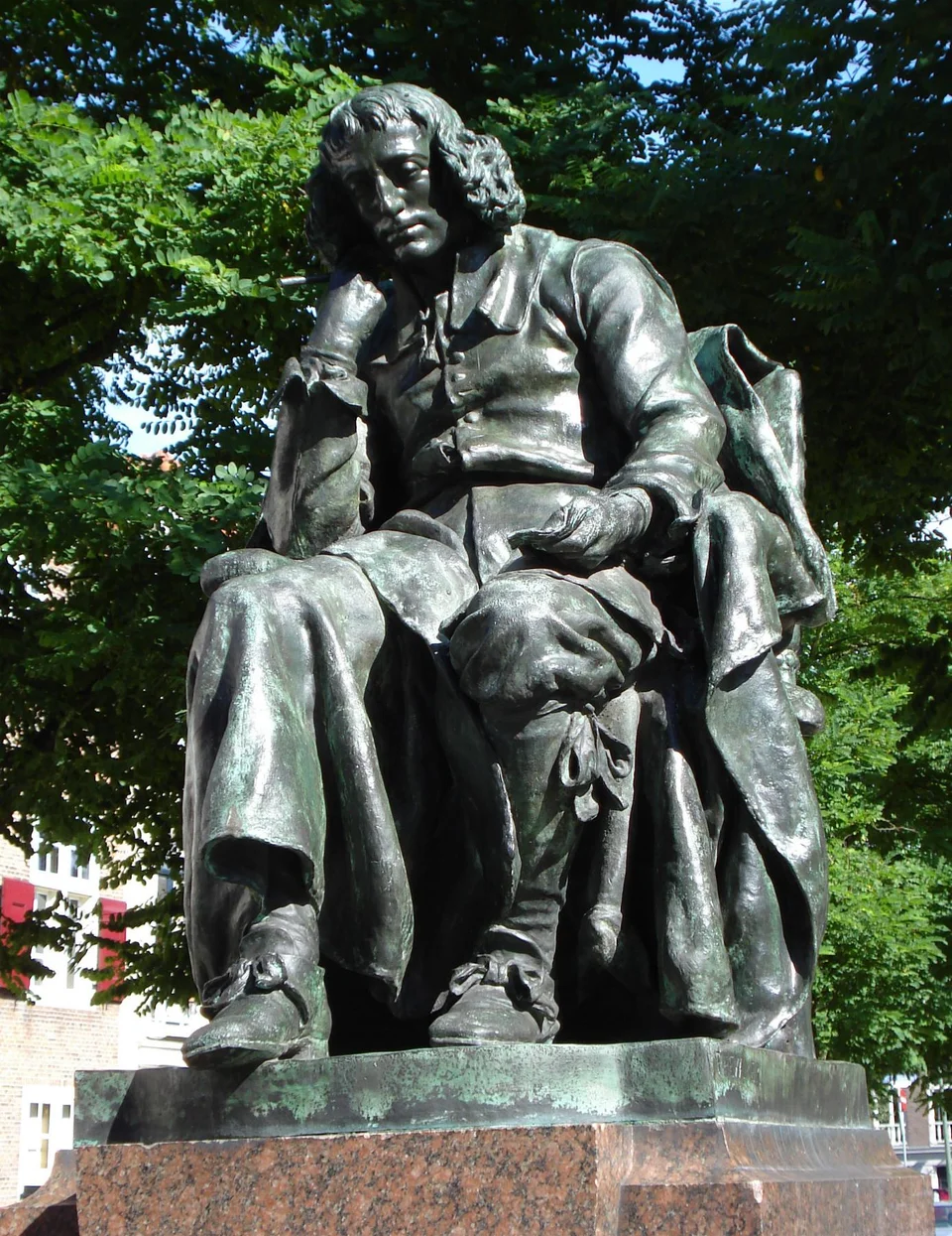 Spinoza als sitzende Bronzefigur auf einem steinernen Sockel in Den Haag